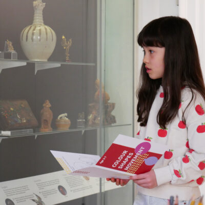 Child holding family trail looking at museum objects.