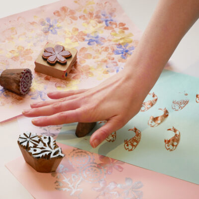 Person pressing stamp onto paper making ink printing patterns in shapes such as fish and flowers