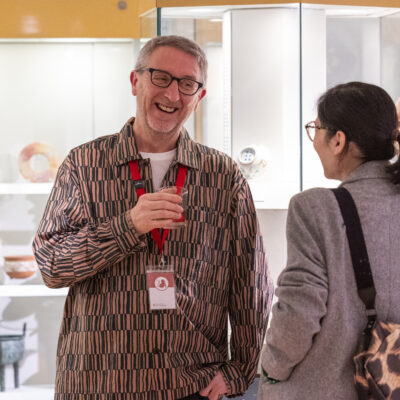 Man smiling in museum gallery space holding glass talking to visitors